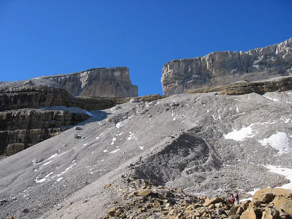 La Brèche de Roland vue d'en bas, entaille entre deux murailles calcaires au-dessus d'un pierrier parcouru de randonneurs