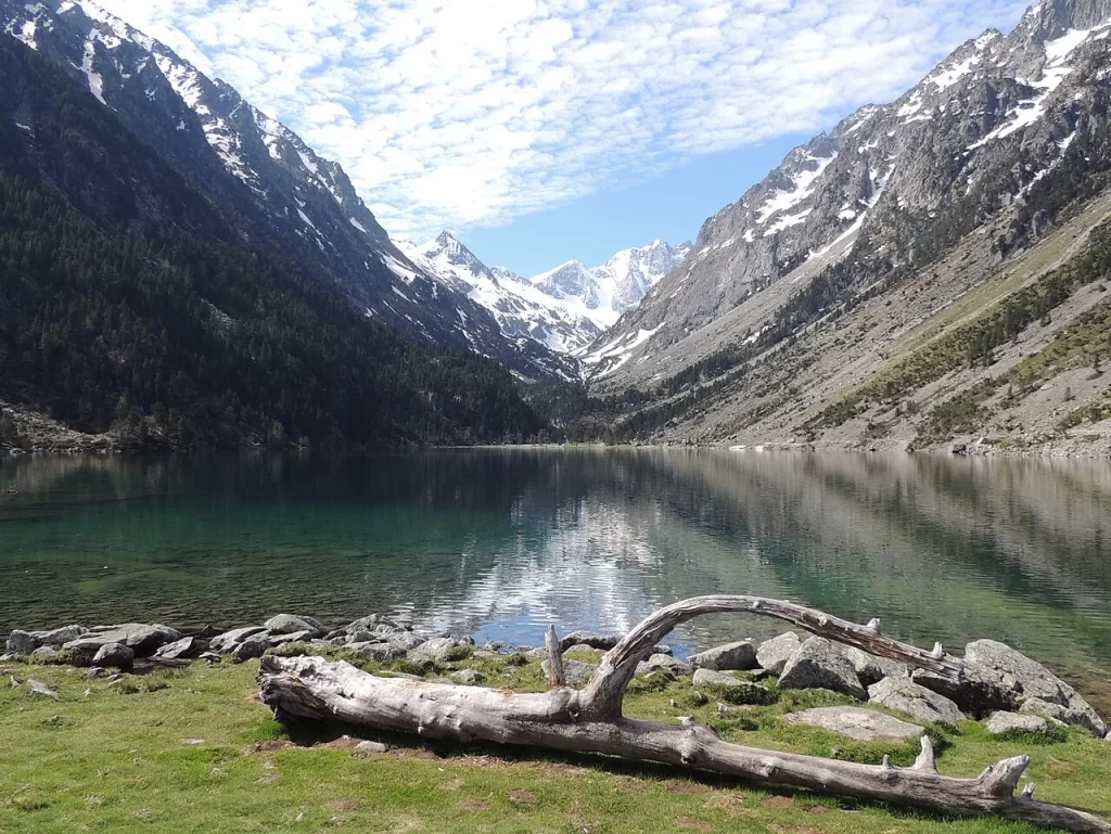 Lac de Gaube aux eaux vertes et calmes, bordé de pentes boisées, avec le massif enneigé du Vignemale au fond de la vallée