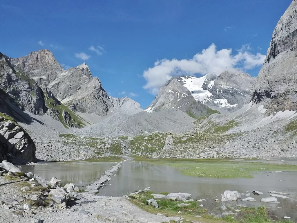 Lac des Vaches traversé par un chemin de dalles, avec la Grande Casse et ses glaciers en arrière-plan