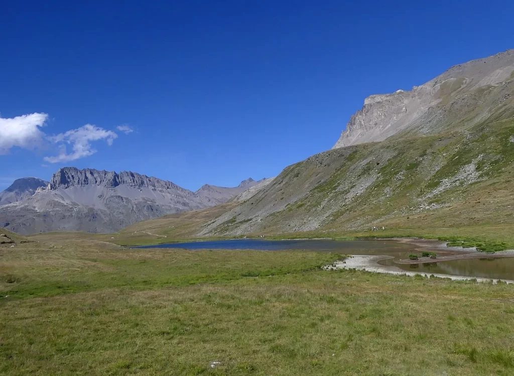 Lac de Plan du Lac au milieu des alpages, entre des sommets rocheux, sous un ciel d'été